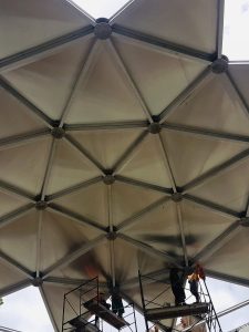 Closeup of the underside of an aluminum geodesic dome with installers on scaffolding