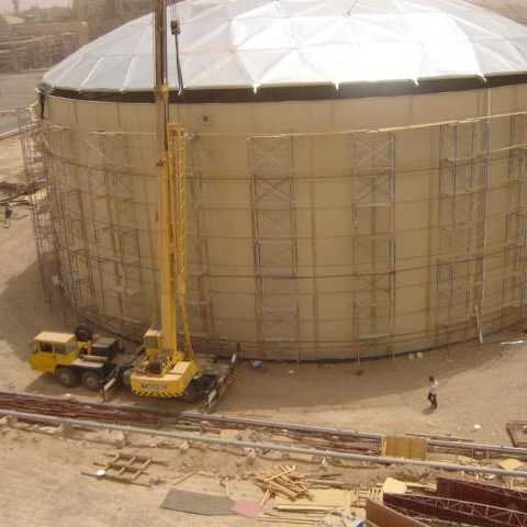 Large Bolted Water Tank with aluminum dome roof. Heavy equipment and dirt job site.