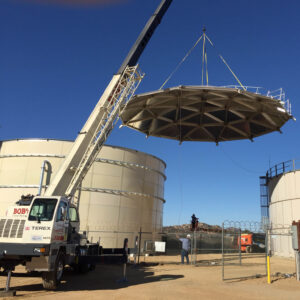 Lifting a geodesic dome atop an tan bolted water tank.
