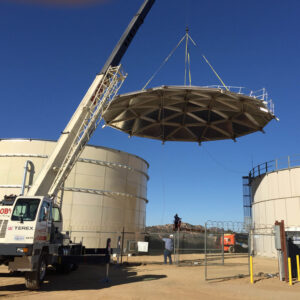 Lifting a geodesic dome atop an tan bolted water tank.
