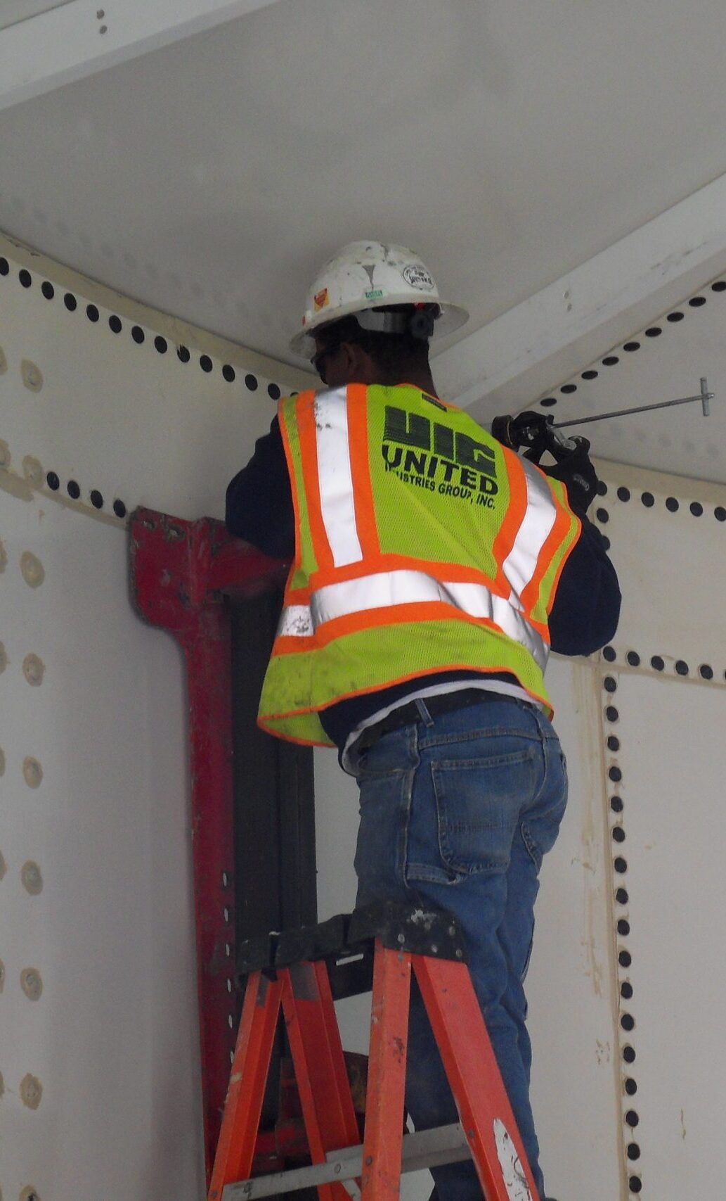 Worker on a ladder applying sealant to panels on a bolted tank
