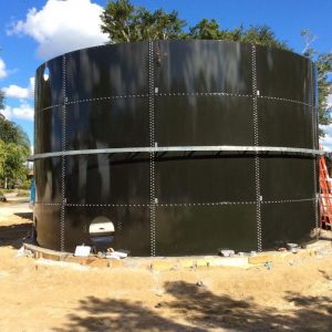 Dark Gray Glass Lined water Tank in a dirt lot. Blue sky and trees.