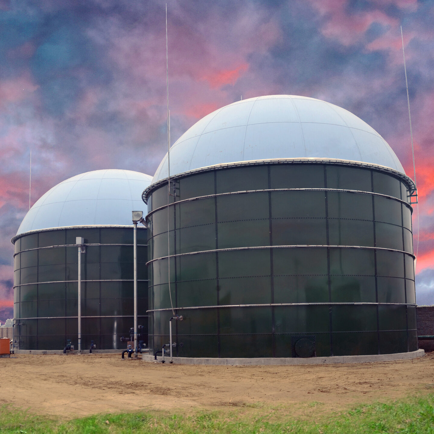 Two Glass Fused to Steel Biogas Storage tanks with white domes and sunset behind. Dirt field and grass in foreground.