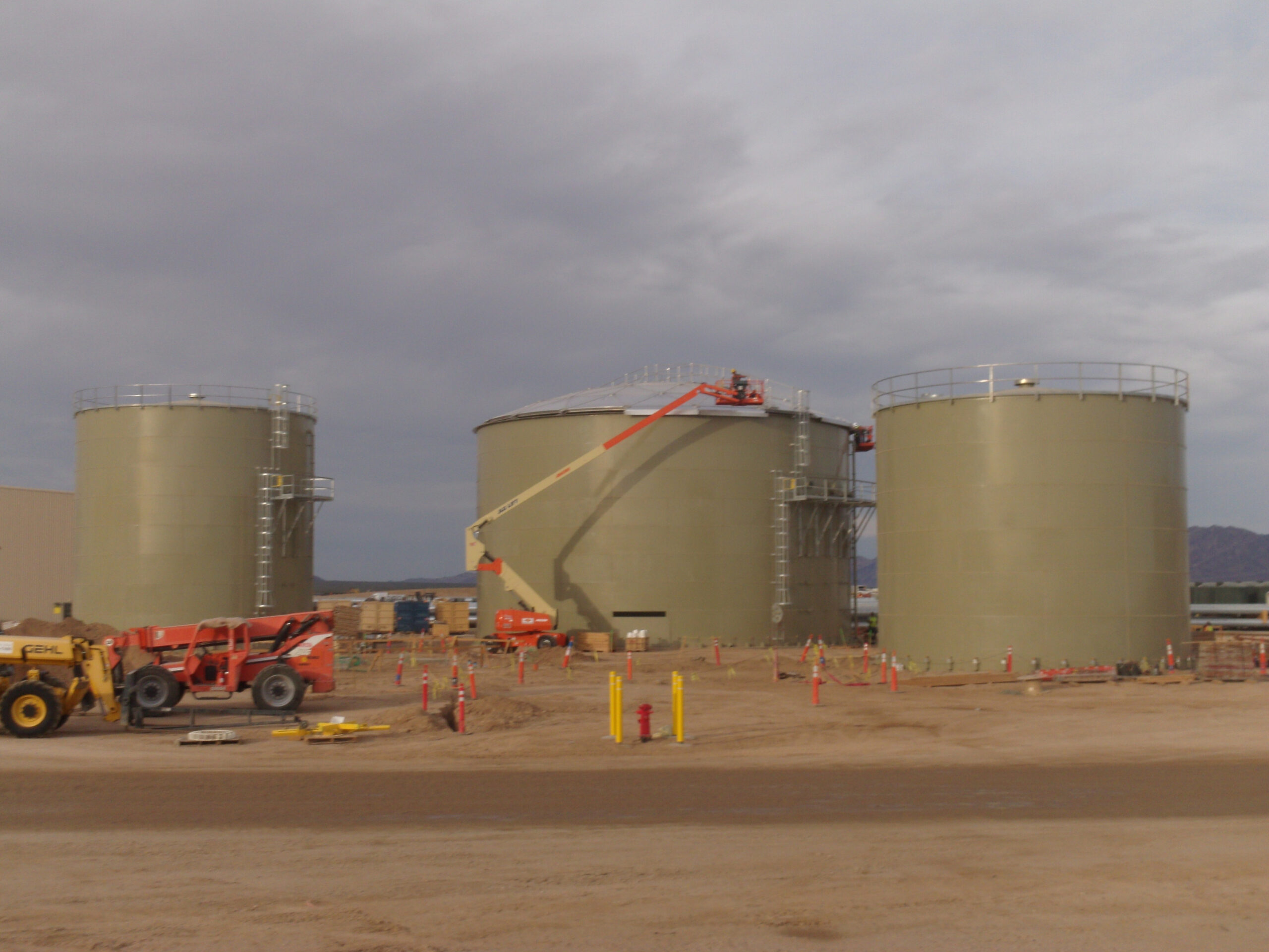 Three Green Bolted Storage Tanks with boom lift in foreground