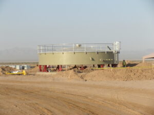 Tan bolted tank walls with red jacks near a dirt driveway