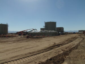 Dirt field with water storage tanks being built using jacks and crane.