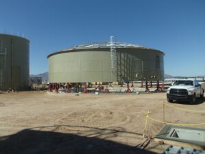 Tank epoxy bolted storage tank on jacks with aluminum dome frame. White truck and second tank in foreground