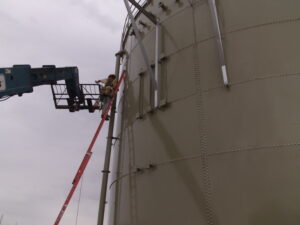 Worker on ladder installing pipe on the side of a bolted water storage tank