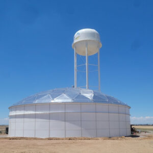 White paneled water tank with dome roof. White Water tank on legs in background.