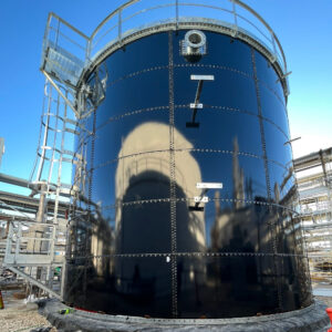 Dark Blue Water Storage tank reflecting another tank. Galvanized tank ladder on left side. Brackets in front of tank