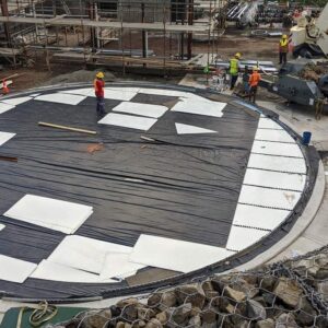 Construction crew laying out white steel panels on a circular concrete pad