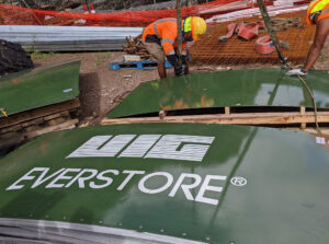 Two construction workers placing straps beneath a green steel panel.