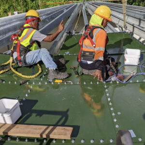 Two workers on top of a green bolted steel tank roof