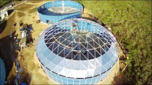 Two empty blue water storage tanks being build with the frame for an aluminum dome roof on top of the closest one.