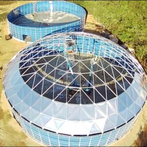 Two empty blue water storage tanks being build with the frame for an aluminum dome roof on top of the closest one.