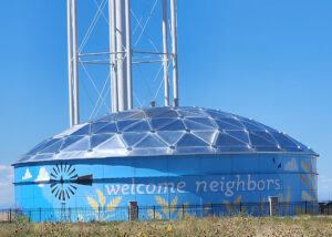 Blue circular water storage tank with the words Welcome Neighbors painted on the side