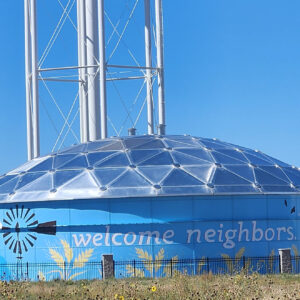 Blue circular water storage tank with the words Welcome Neighbors painted on the side